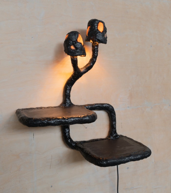 A metal light mounted on a wall with two small integral shelves