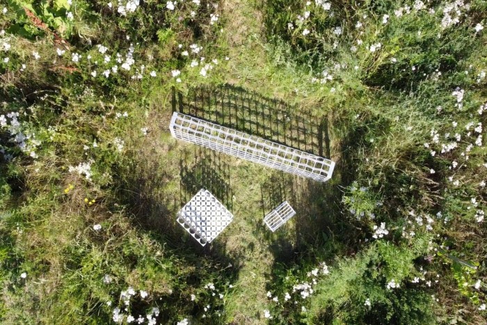 Pieces of furniture made from white metal grids photographed from above in a meadow