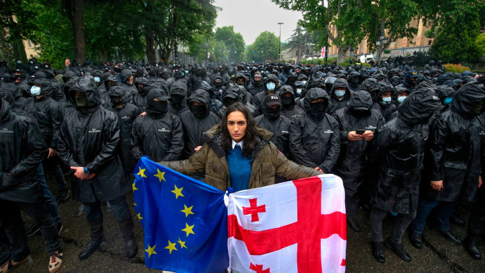 A female protester holds both an EU and a Georgian flag in front of riot police in Tbilisi on Tuesday