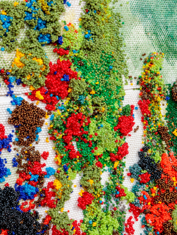 A beaded artwork gathers painted glass beads in the tones of green, red, blue and yellow into an abstract, cloud-inspired composition