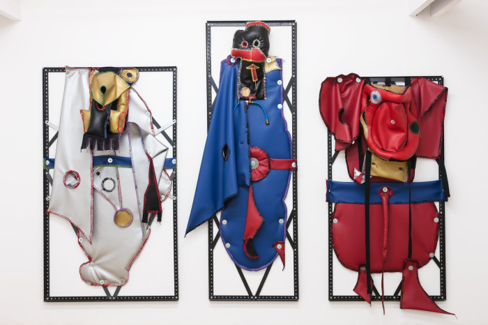Three black metal frames each with a red, white or blue rubbery costume/figure hanging from it