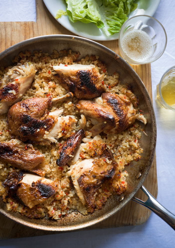 A frypan contains rice with bits of cooked chicken on top