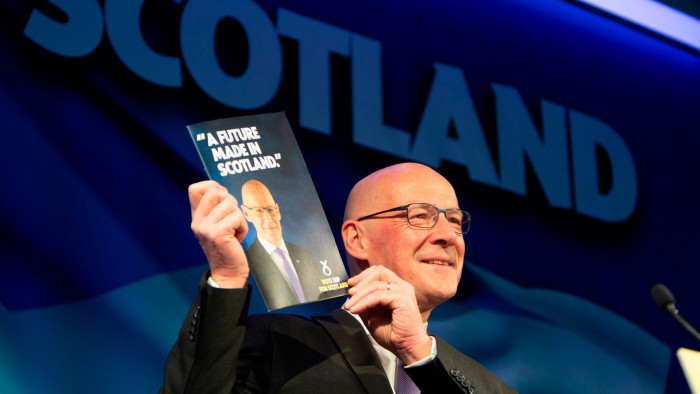 John Swinney smiles as he holds up a copy of the SNP election manifesto