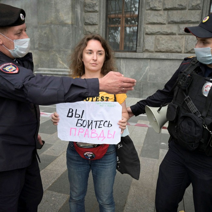 A young woman stands holding a sign, with two police officers waving their arms near her