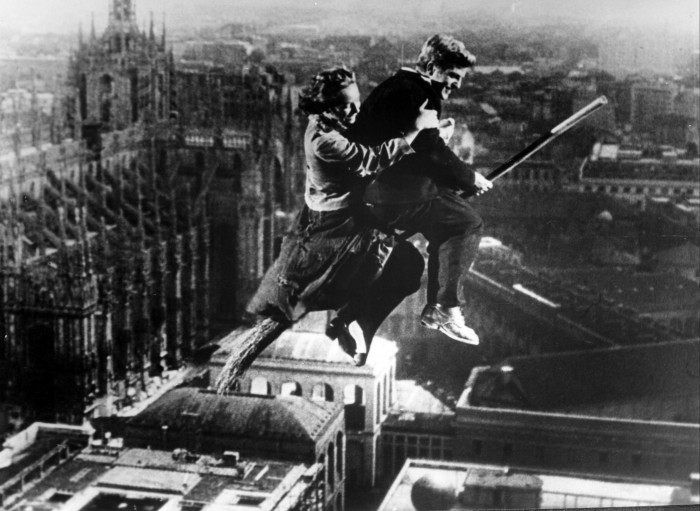 A man and a woman sitting on a broomstick flying over the city in a scene from ‘Miracle in Milan’