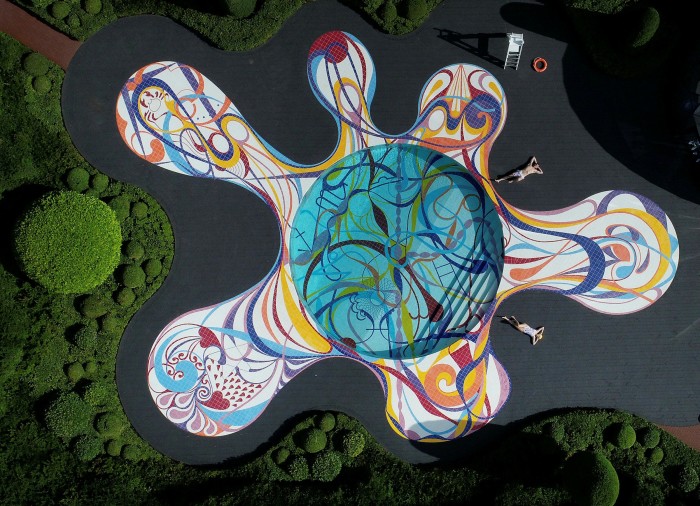 A circular swimming pool incorporating and surrounded by a loopy colourful design in its tiles
