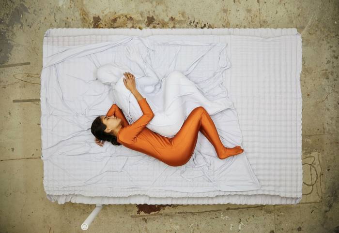 A person in a bronze bodysuit spoons a figure in white on a bed