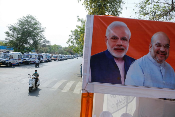 A long line of ambulances carrying Covid patients waits outside a hospital, within sight of portraits of Narendra Modi and his deputy Amit Shah