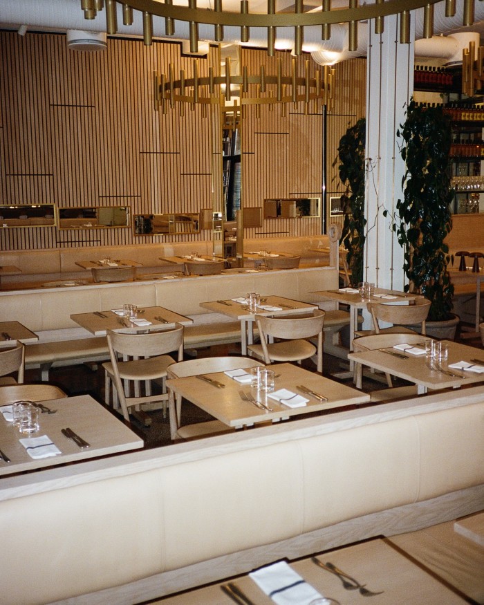 The blond-wood interior of Aamanns 1921, with tables close together and modern gold chandeliers 