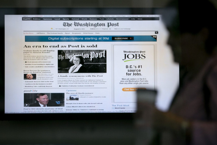 A woman walks past a monitor displaying news that the owners of the Washington Post are to sell the newspaper to billionaire Jeff Bezos inside the Washington Post headquarters in 2013 