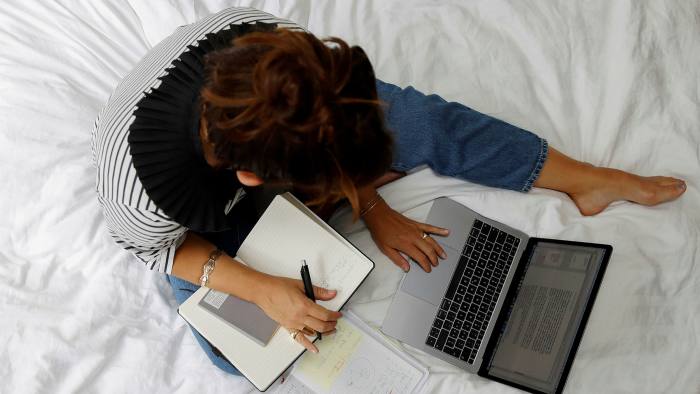 Person, with laptop, notes and pen, working on a bed