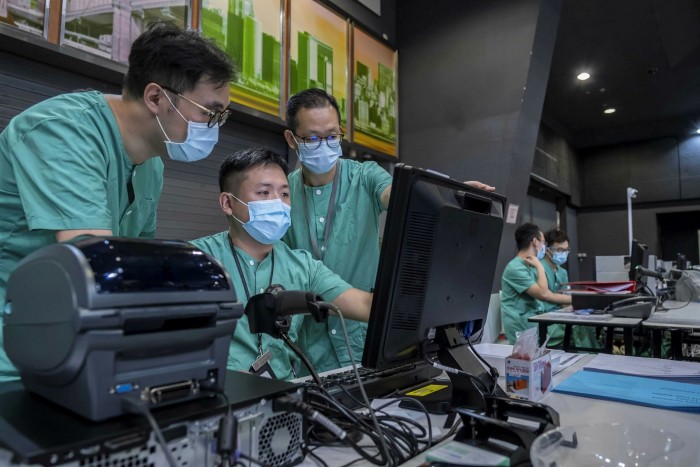 Health workers wearing protective masks look at a computer during a media tour of a temporary community treatment facility for Covid-19 patients at the AsiaWorld-Expo