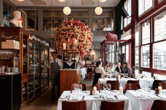 Seating inside Bistro Boheme, with a gigantic vase of red and cream flowers beside the tables, and large windows to the right