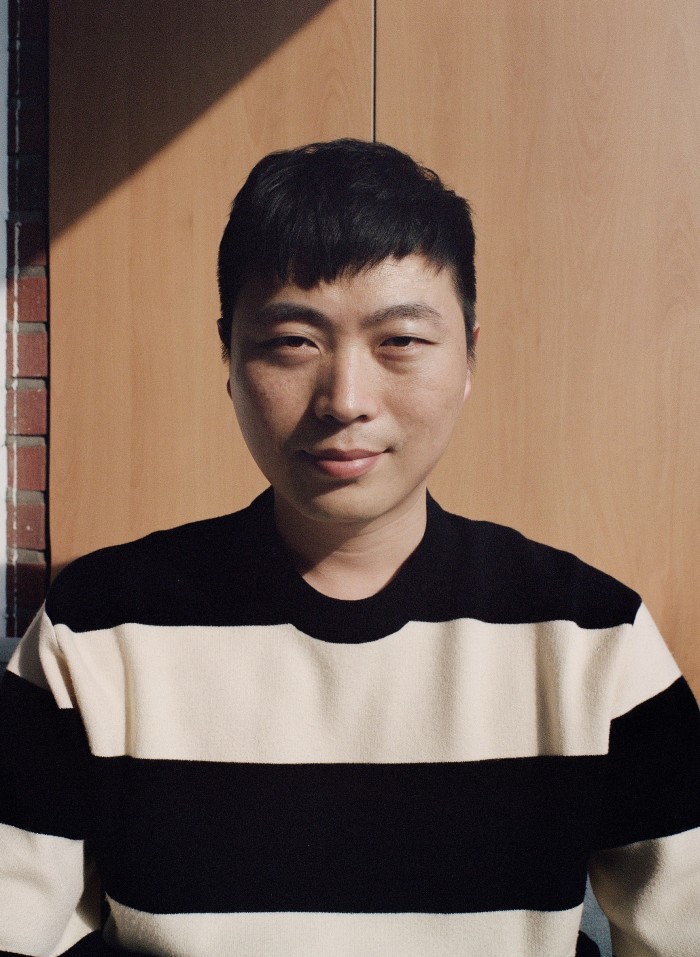 A close-up portrait of Jang Hyeok, looking straight into the camera. He wears a black and white striped jumper  
