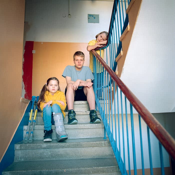 Denys is sitting on the landing halfway up the stairs, Zosia sits on a step below him, Janek is leaning on the handrail