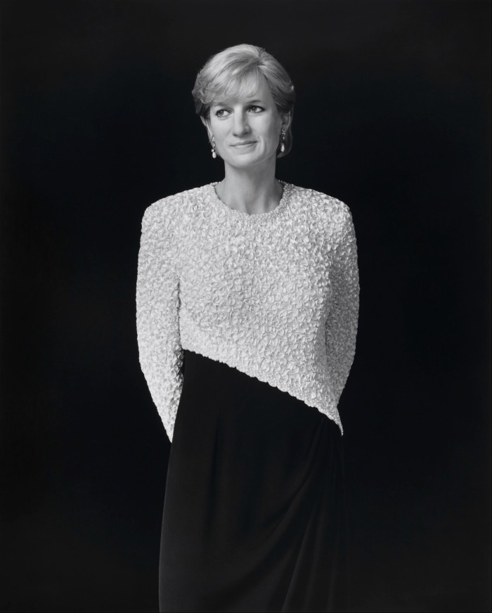 In a monochromatic photograph, a young woman wearing pendant pearl earrings and a black-and-white dress with an asymmetric motif looks to her right 