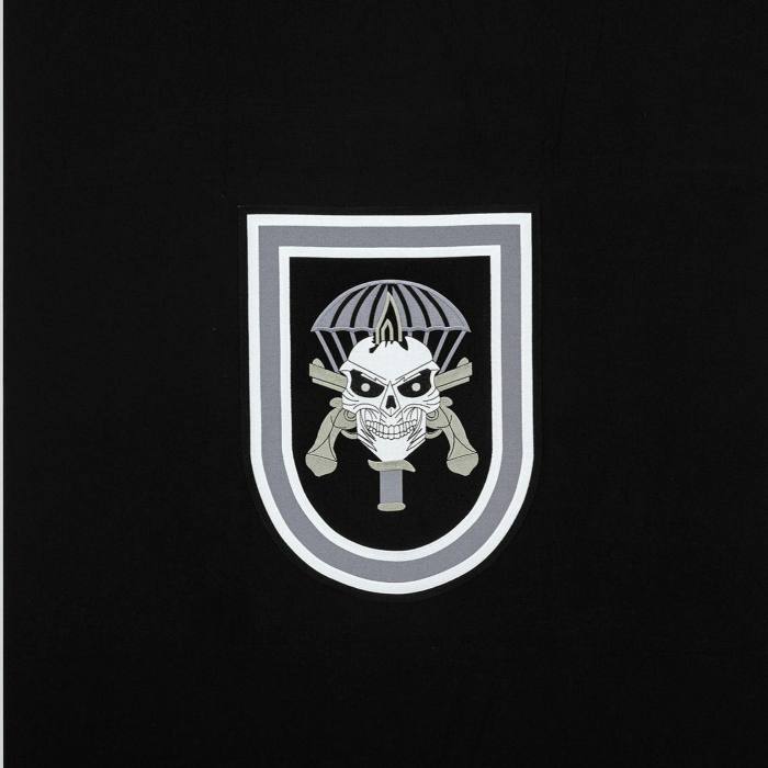 Embroidered emblem of a skull pierced with a dagger overlays a pair of crossed guns and a parachute, against a black background