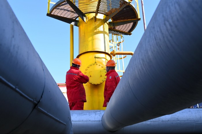 Two workers examine a vertical tube which is connected to a number of pipes