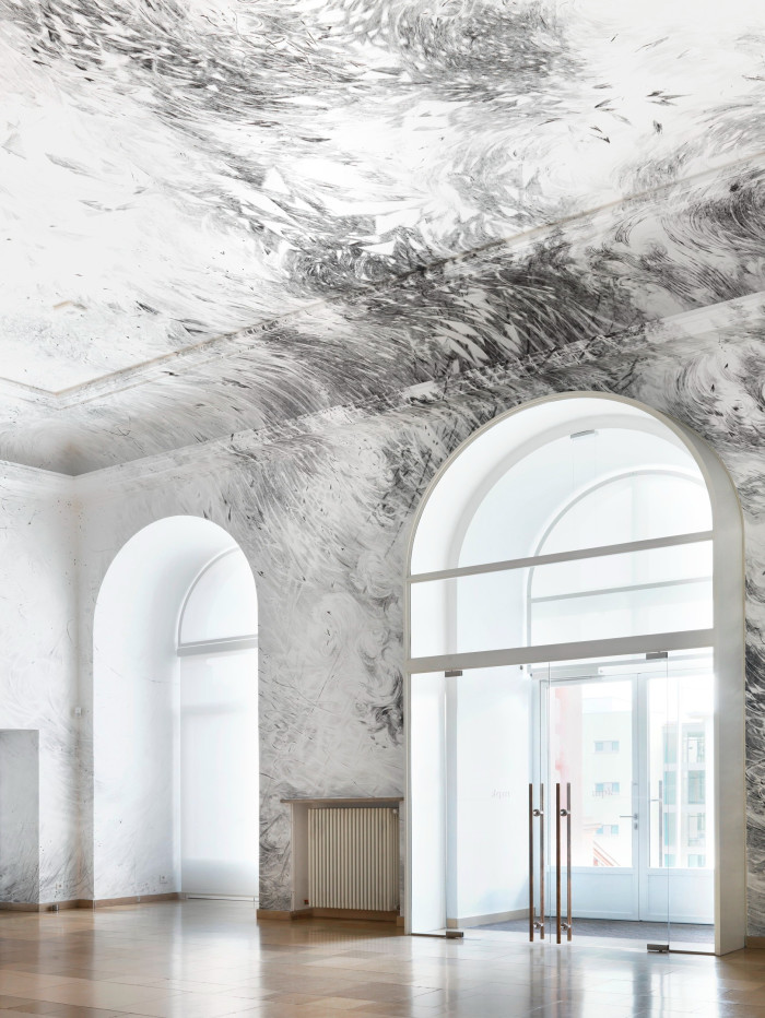 A black and white abstract composition resembling crashing waves expands over the white ceiling of a brightly lit room decorated with arched windows