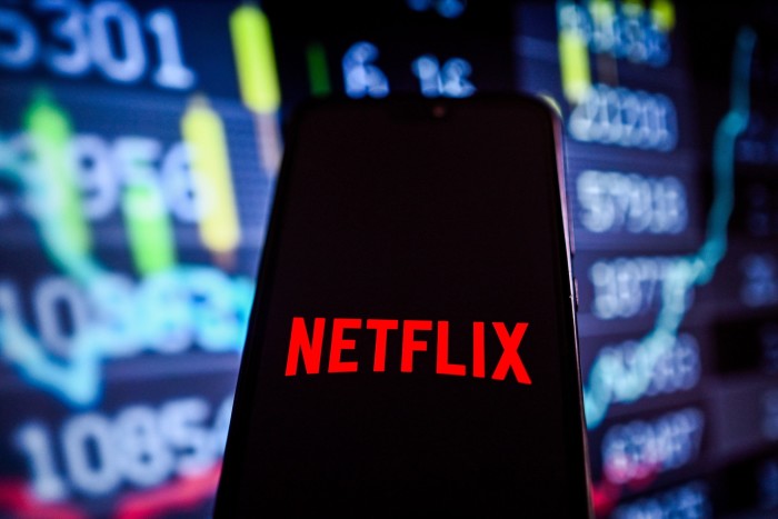 A Netflix logo is displayed on a smartphone with stock market percentages on the background