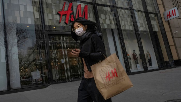 A woman with an H&M shopping bag walks outside an H&M store in Beijing