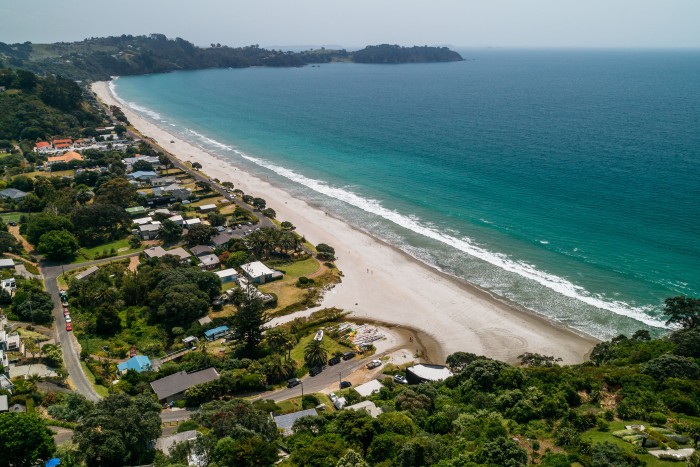 An aerial view of Onetangi beach: houses and greenery, white sand, blue-green sea