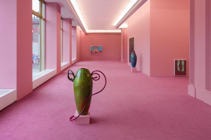 A slim tall green vase stands on pink carpet in a room with pink walls