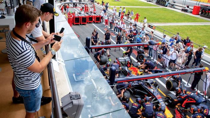 Two people with mobile phones taking pictures of a racing car while in a Formula One pit stop