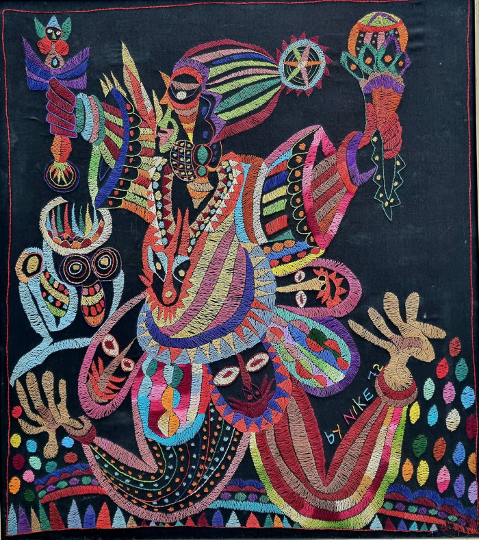 A bright tapestry work in every kind of colour of a human figure holding up rattles