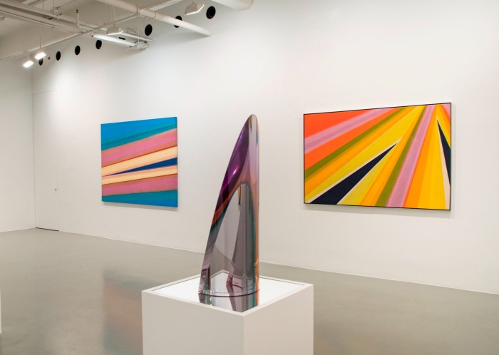 Two large colourful abstract canvases hang on a wall with a transparent, pointed sculpture on a pedestal in front
