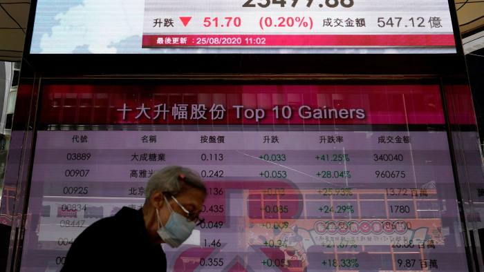 A woman wearing a face mask walks past a bank’s electronic board showing the Hong Kong share index at the Hong Kong Stock Exchange on Tuesday