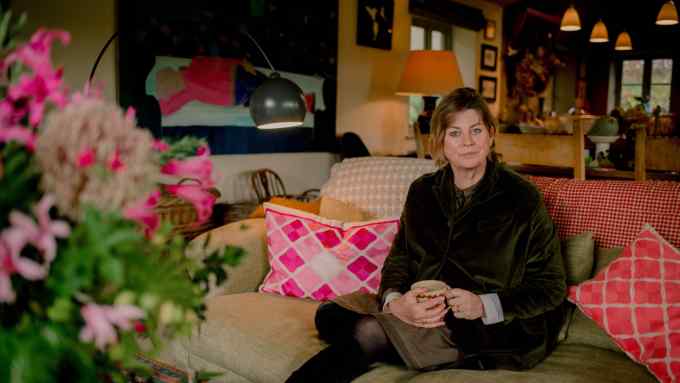 A middle-aged woman sits on a sofa in the lounge of a country house