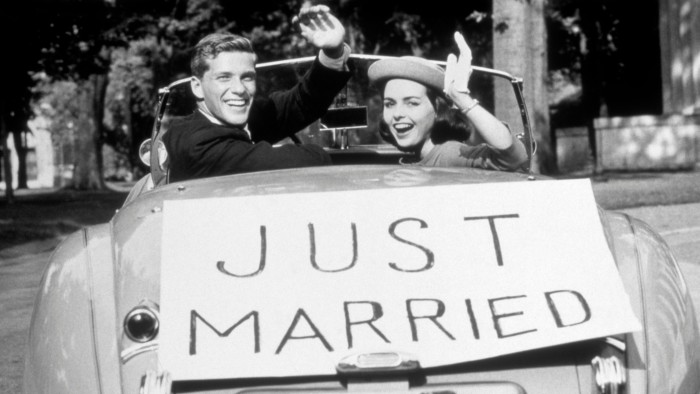 1950s shot of a couple with a ‘Just Married’ banner on the back of their car 
