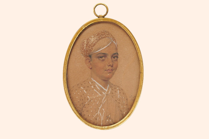 A golden, oval-shaped pendant contains a painted portrait of a dark-eyed teenage boy dressed in a silky, elegant shirt and matching headpiece.