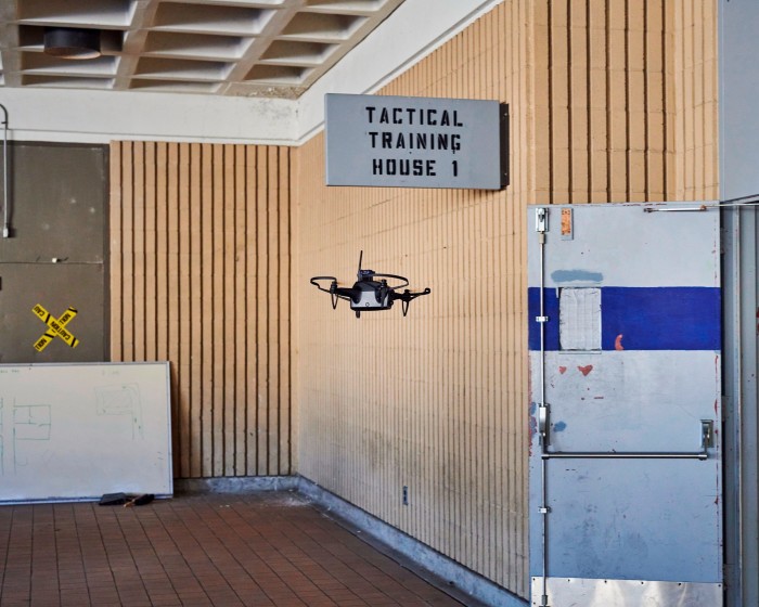 A drone flies in a room where there is little other than a sign saying Tactical Training House 1