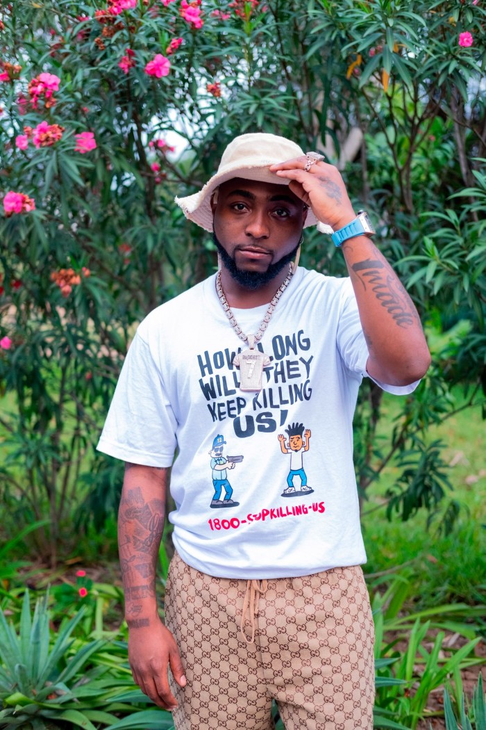 Afrobeats singer Davido in Accra, Ghana, wearing a T-shirt and hat and surrounded by trees and flora 