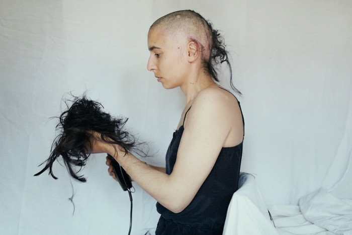 A woman with shaved head holds her hair in her hands