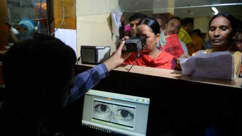 An Indian woman looking through an optical biometric reader during registration for an Aadhaar card