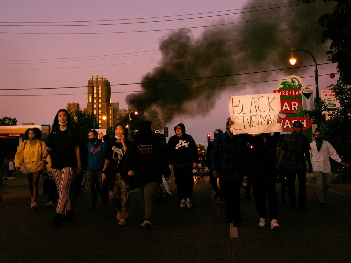 Protesters march in Minneapolis as smoke rises behind them