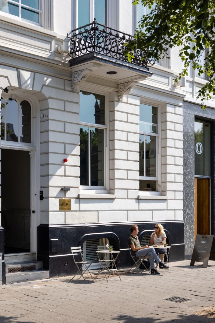 The white-brick facade of the Hotel Âme, with a man and a woman sitting at a table on the pavement outside