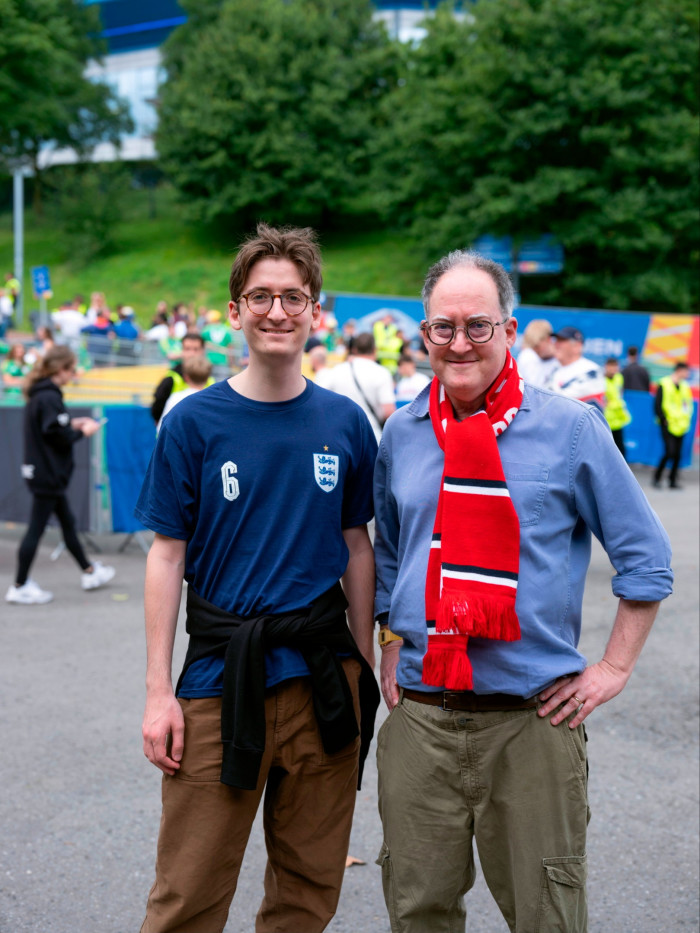A smiling man in glasses, wearing an England scarf, stands next to a younger man who wears an England football shirt
