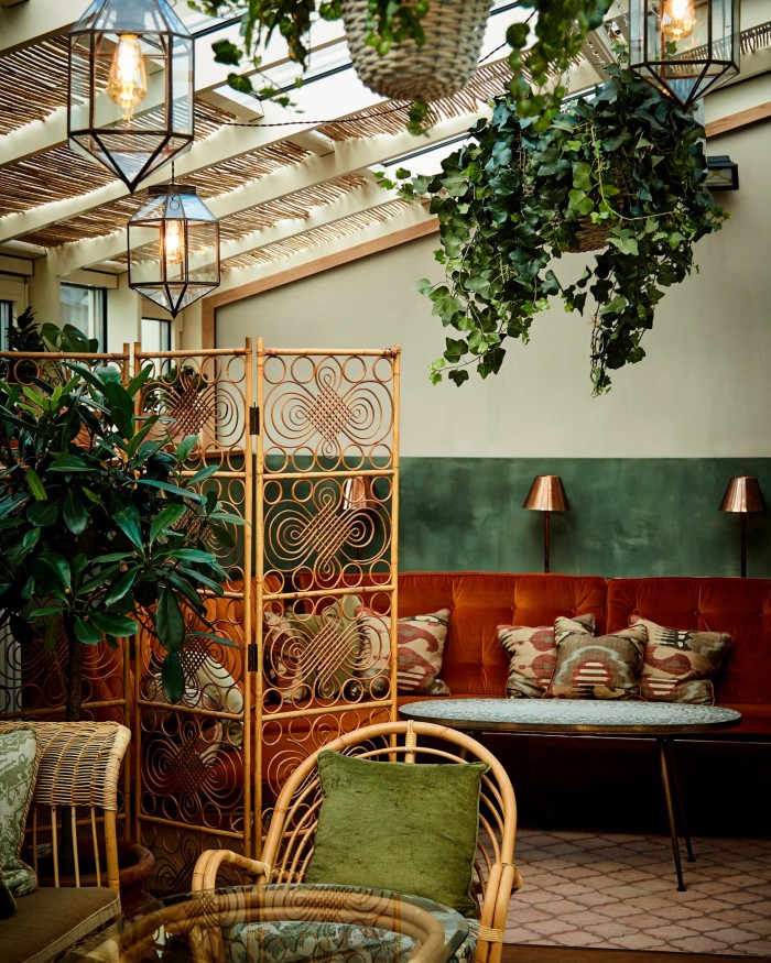The hotel’s roof terrace, with a red velvet banquette, rattan chairs and screens, and plants hanging from the ceiling 