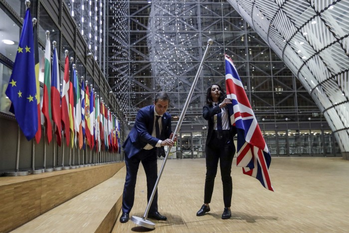 Two staff members lower the union flag from a pole. Beside them is a wall of flag poles