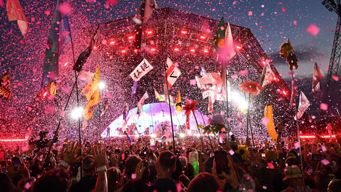 A large rock concert stage is surrounded by flags, fireworks, confetti and lights