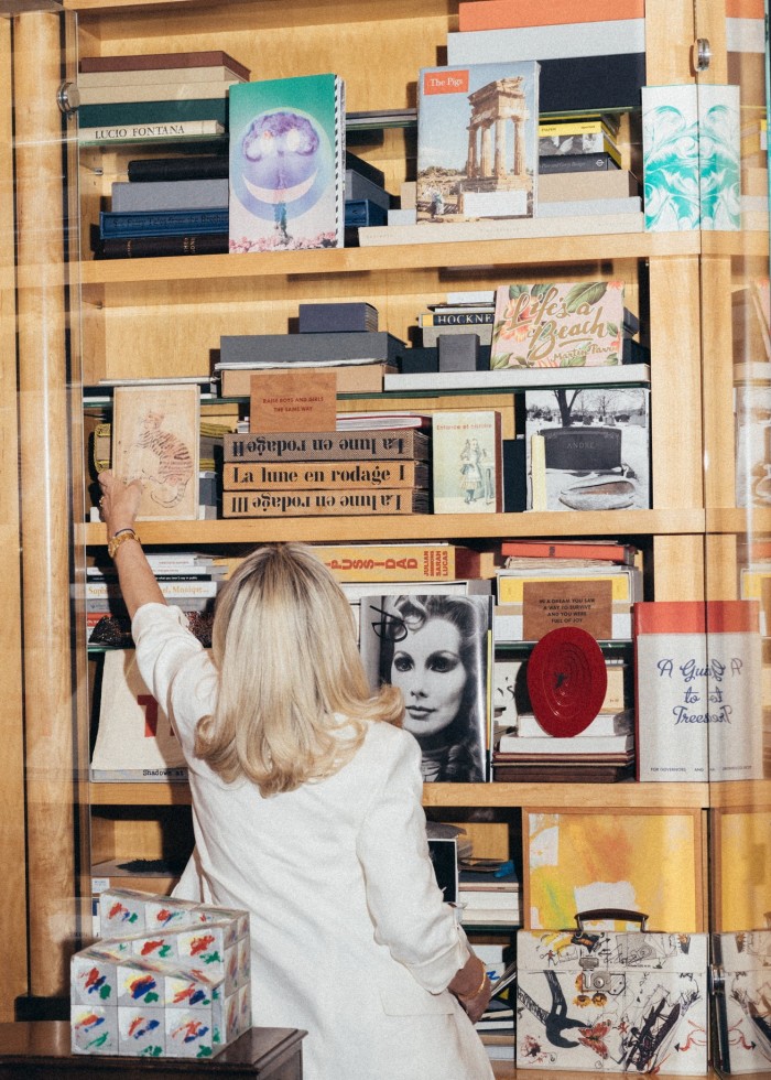 A blond woman reaches up for a book in a set of shelves