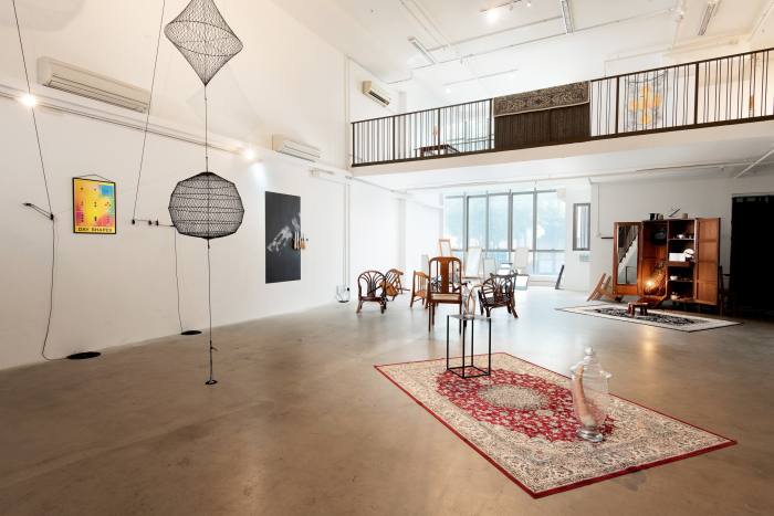 A gallery space with an interior balcony. The floor is bare concrete except for two carpets, and most exhibits relate to or contain items of furniture