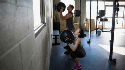 G0MGNY Man and woman squatting with medicine balls gym