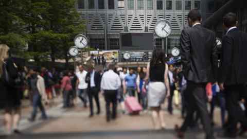 Office workers pass clocks in front of No. 1 Canada Square, or Canary Wharf Tower, in this photograph taken on a tilt-shift lens in the Canary Wharf business and shopping district, in London, U.K., on Friday, July 12, 2013. Recent data suggest Britain's economic recovery is gaining momentum after a return to growth in the first quarter. Photographer: Simon Dawson/Bloomberg