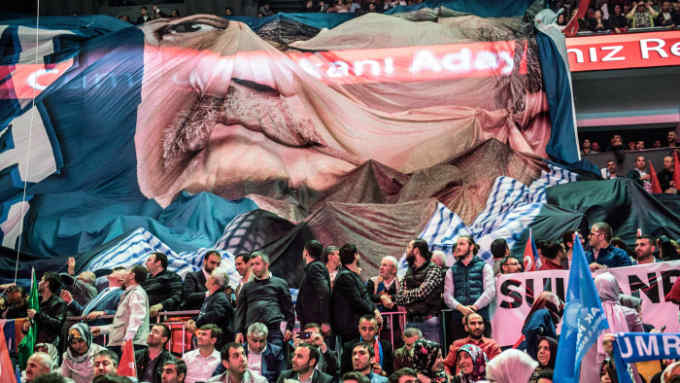 Supporters of Turkey's President Recep Tayyip Erdogan (on banner), unfurl his image as he gives his speech presenting his People's Alliance election strategy in Istanbul on May 6, 2018. - Turkey will hold parliamentary and presidential elections on June 24, 2018, seen as important as it will transform Turkey's governing system to an executive presidency. The main opposition Republican Peoples Party (CHP), the IYI (Good) Party, the conservative Saadet Party (SP) and the Democrat Party (DP) formed the Alliance for the Nation to stand against the People's Alliance of Erdogan's ruling Justice and Development Party (AKP) and the Nationalist Movement Party (MHP). (Photo by BULENT KILIC / AFP) (Photo credit should read BULENT KILIC/AFP/Getty Images)