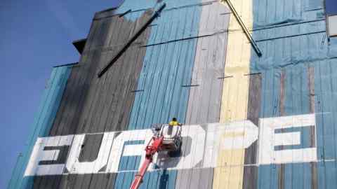 An artist stands on a cherry picker to work on a mural next to the European commission and the Europa building in Brussels, Belgium, on Thursday, June 22, 2017. EU leaders are expected to reaffirm their commitment to &quot;robust&quot; free trade and the Paris Agreement on climate change when the two-day meeting concludes on Friday. Photographer: Jasper Juinen/Bloomberg
